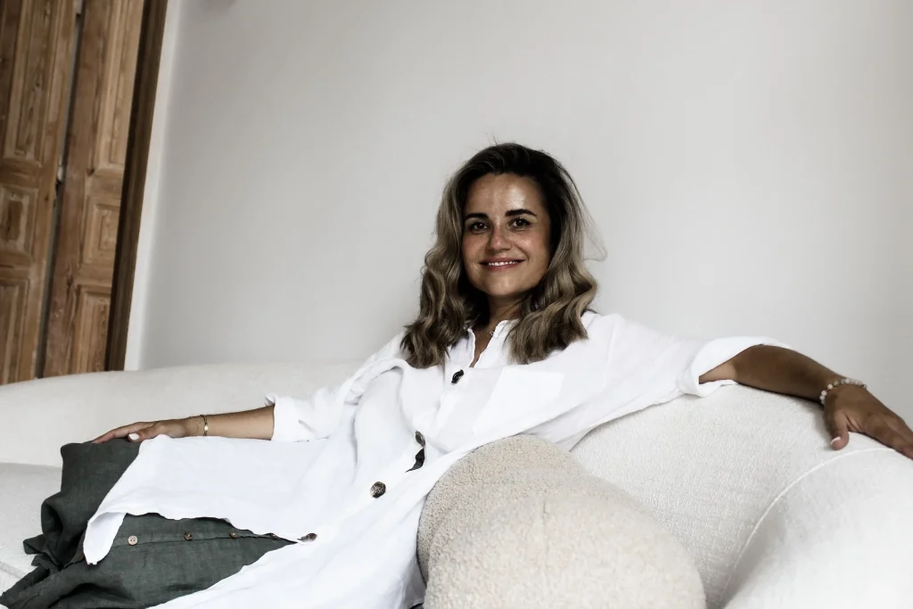 Dr. Dominika smiles while sitting on a white couch.