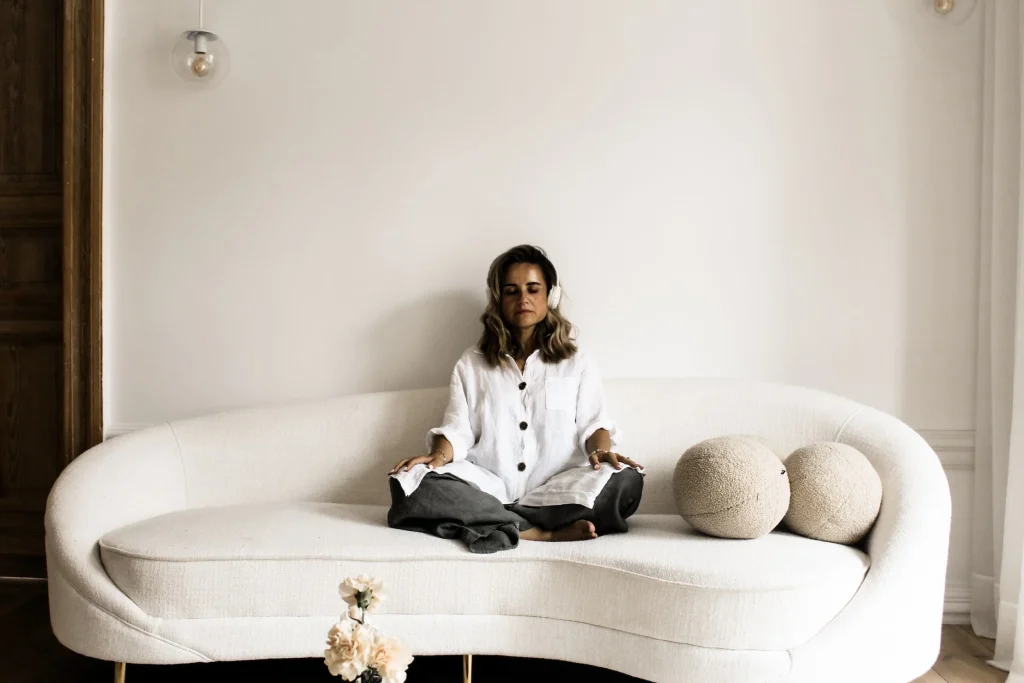 Dr. Dominika sits on a white couch and meditates while wearing headphones.